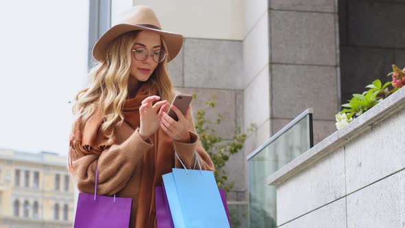 Young Girl Online Typing on Telephone Female Shopper Stands in City with Shopping Bags Caucasian