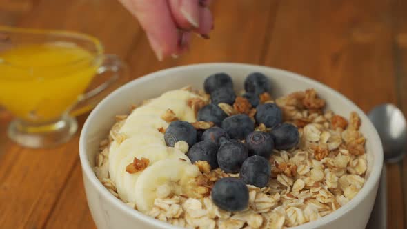 Closeup of a Woman's Hands Sprinkling Flax Seeds on a Plate of Oatmeal