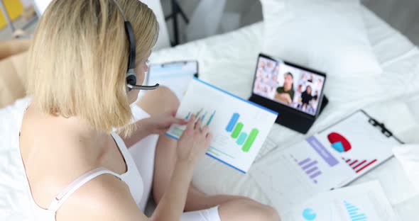 Woman Operator Earpiece and Microphone Sits on Bed and Holds Online Conference