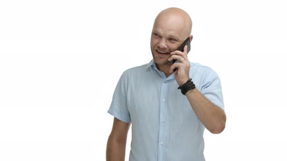 Cheerful Middleaged Bald Man with Beard Wearing Bracelets and Shirt Talking on Mobile Phone Having