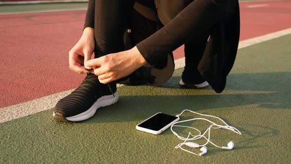 Young Athlete Woman Tying Running Shoes with Earphones on the Ground. Close Up