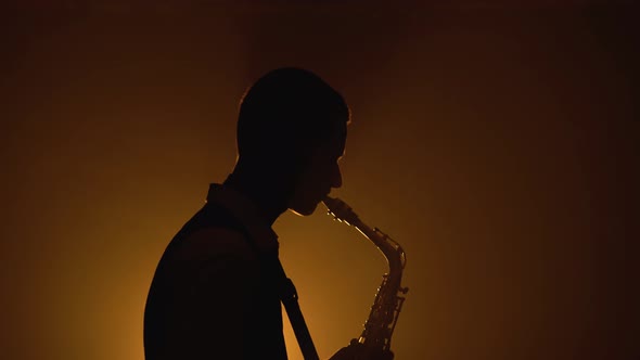 Silhouette a Young Stylish Guy Plays the Golden Shiny Saxophone in the Yellow Spotlights on Stage