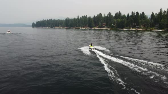 Drone shot following a person driving a jet ski at Payette Lake in McCall, Idaho with the shore and