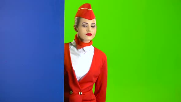 Girl Looks Out From Behind the Blue Board and Points at Her Hand . Green Screen