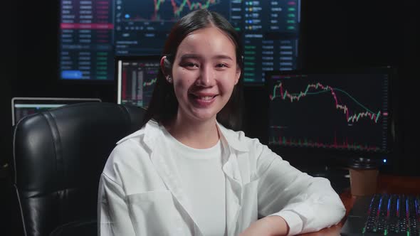 Asian Female Stock Market Broker Working On Computer And Smiling To Camera