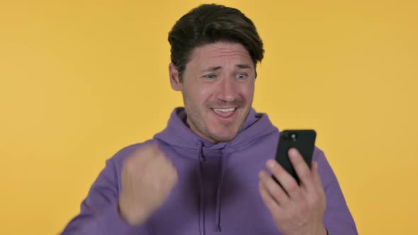 Man Celebrating on Smartphone, Yellow Background 