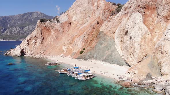 Drone Shooting of the Orange Volcanic Mountains of Suluada Island and the White Beach with Tourists