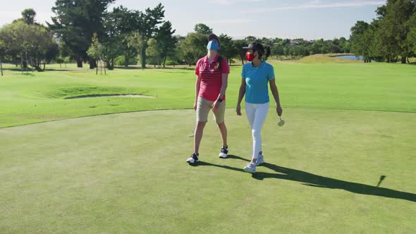 Two caucasian women playing golf wearing face masks walking together