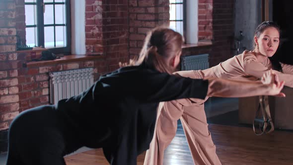 Two Women Warming Up Together in Front of Each Other Before Sports Training in the Gym