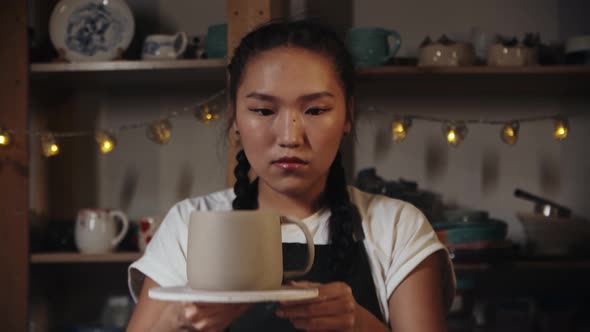 Young Woman Potter Trying on a Wet Clay Handle to a Cup and Looking at It