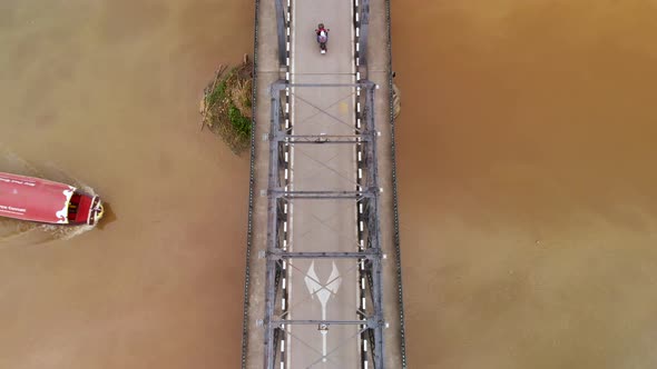 Aerial drone view of vehicles driving over bridge while Thai river boat passes below in Chiang Mai T