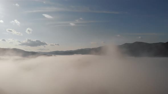 Aerial Drone Flight View Over Low Clouds and Morning Mist Covered Mountain Slopes at Sunrise