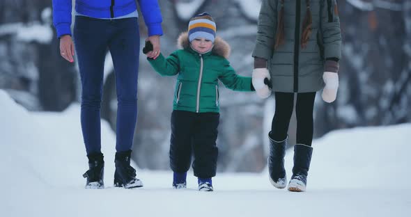 Happy Baby Walking with His Sister and Mother in the Winter Park