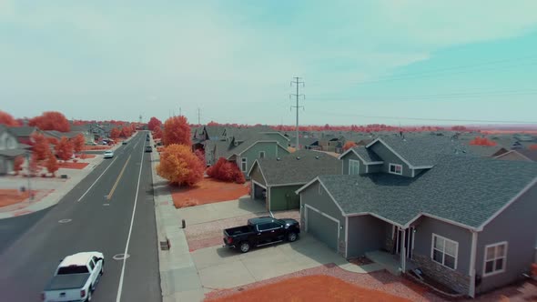 A near infrared drone rises above a neighborhood with two trucks breaking the right of the screen dr