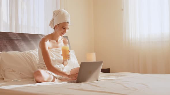 Young Girl with Long Hair in White Robe Using Laptop Having Breakfast Orange