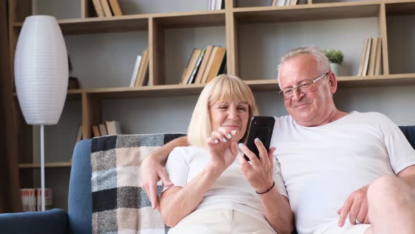 Happy Senior European Pensioner Couple Holding Smartphone Laughing Looking at Funny Photos