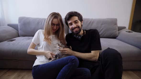 Beautiful Young Couple with Their Cat on Their Living Room Couch Talking to the Camera