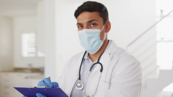 Portrait of hispanic male doctor having interview with patient at home wearing face mask