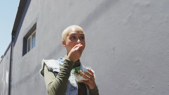 Mixed race woman walking on street and eating a takeaway salad lunch