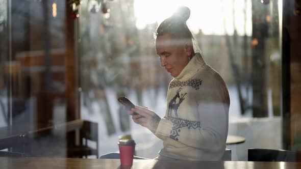 A Cute Gay Gay Man is Sitting in a Cafe with a Phone