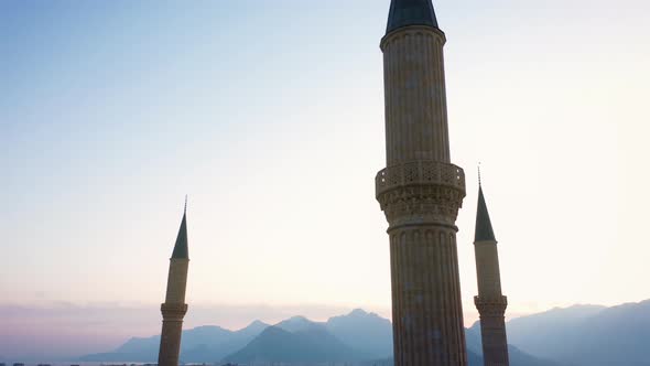 Islamic Mosque Minarets on Sunset Sky and Mountains Background