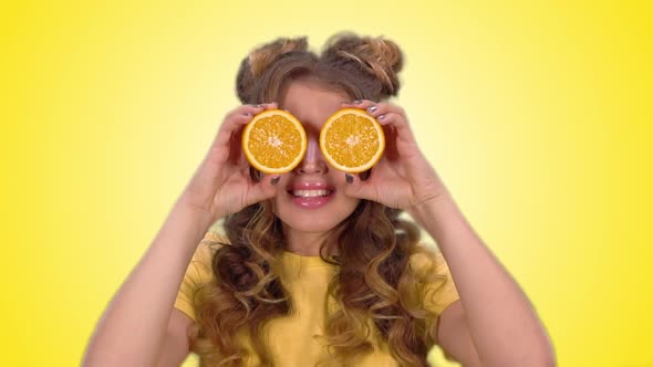 Beautiful Young Girl in a Yellow Vest Posing with Oranges and Smiling While Looking Into the Camera