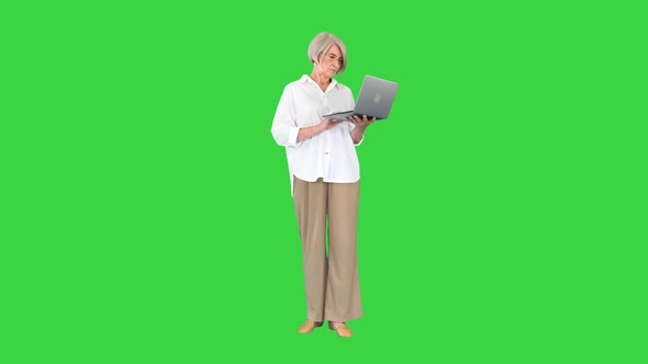 Grey Haired Satisfied Mature Woman Using Laptop Standing on a Green Screen Chroma Key