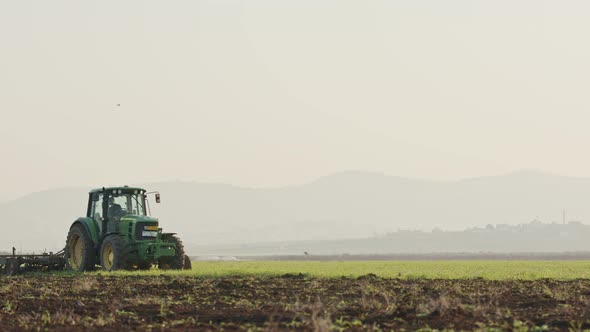 Tractor cultivating a green field in slow motion.