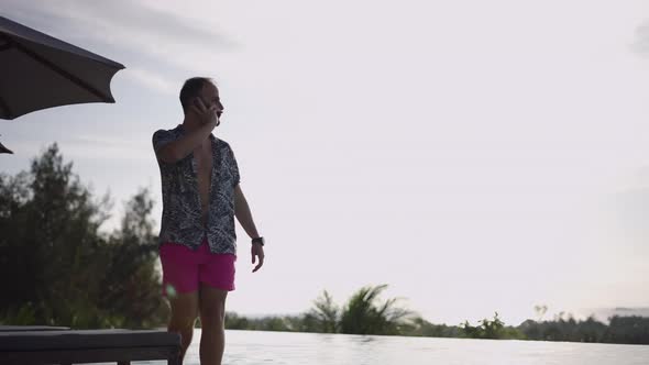 Bearded Caucasian Man Walking Along the Infinity Swimming Pool While Talking on a Mobile Phone