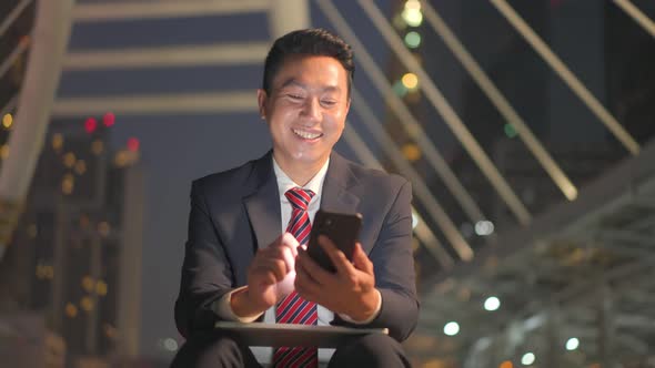 Asian businessman working by using moblie phone chat with colleagues team at night in city.