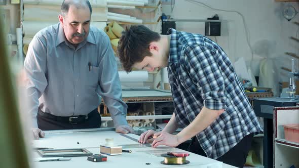 Young Trainee Constructing a Frame Behind the Desk in Frame Workshop