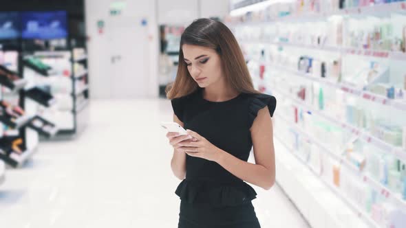 Front View of Young Caucasian Woman is Chatting on Her Smartphone in Store