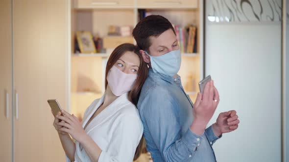 The Family Checks for News Related To the Coronavirus. Quarantining at Home. A Couple Wears Masks