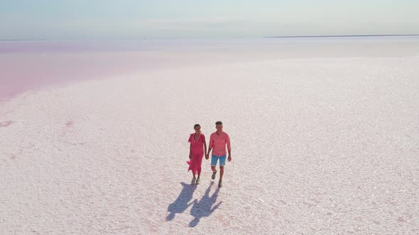 Aerial Epic Drone Image of Lovely Romantic Couple Walking Along Bright Colorful Pink Water of