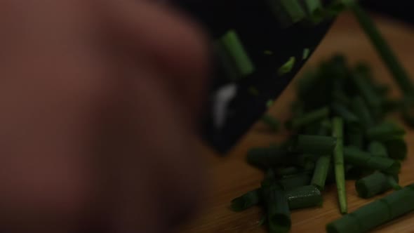 Macro shot of gathering sliced green spring onion pieces on a wooden chop board with a knife