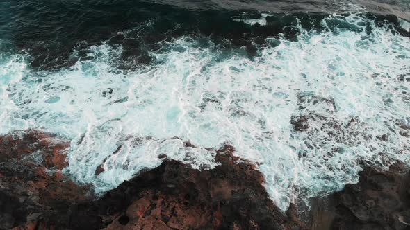 Aerial view Big ocean waves hitting and spreading over rocky beach creating white foam and splashing