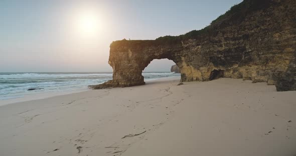 Sun Over Natural Hole in Cliff Wall on Sand Ocean Shore Closeup Aerial