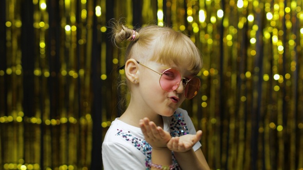 Child Smiling, Looking at Camera, Making Fly Kiss. Girl Posing on Background with Foil Curtain