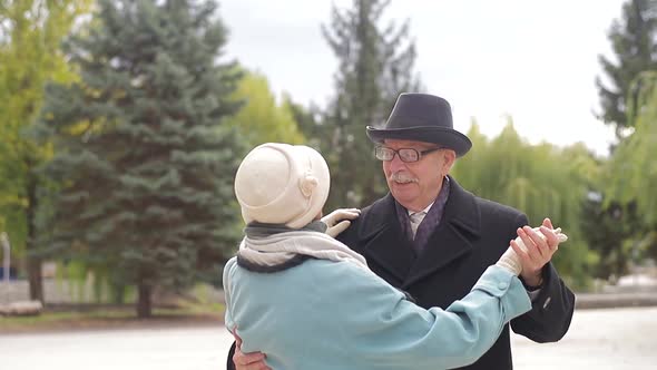 Old European man and woman dancing together in park standing.