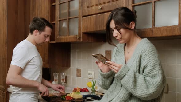 Young Man Prepares Food in the Kitchen While His Wife Is Surf the Internet