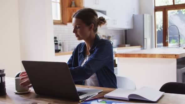 Woman with coffee cup using laptop in the kitchen