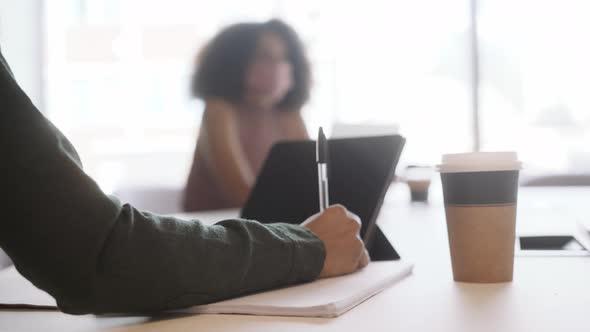 Businesswomen Wearing Masks Making Notes In Socially Distanced Meeting In Office During Pandemic