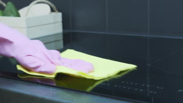 Woman in pink rubber gloves cleaning cooking panel with fat remover spray and a duster