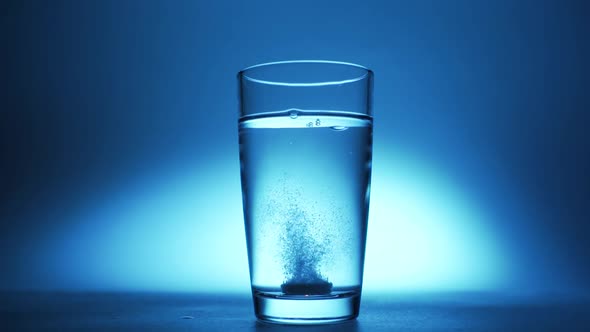 An Effervescent Soluble Tablet Falls Into a Glass of Water. On a Blue Background