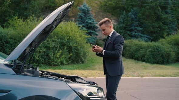 Male Driver with Smartphone Modern Car Looking on Breakdown Hood of Vehicle