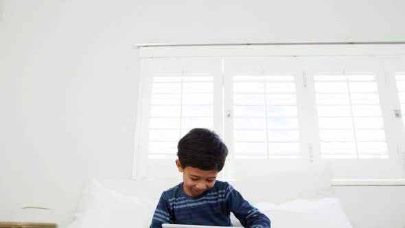 Boy using digital tablet while relaxing on bed