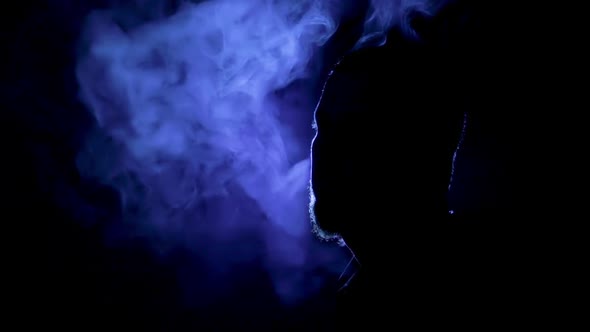 Silhouette of man smoking on black background with blue light, reverse video
