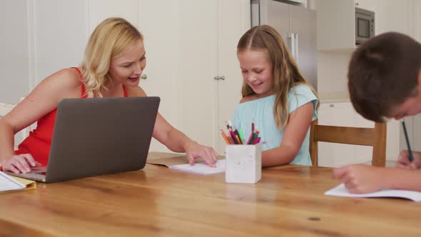 Caucasian mother helping her daughter with homework while using laptop at home