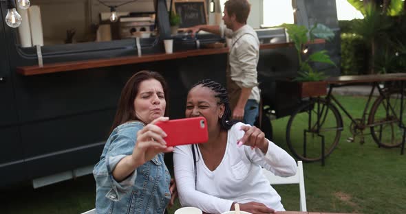 Multiracial women having fun taking photos with mobile phones at food truck restaurant outdoor