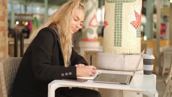 Freelancer woman writing notes while working with laptop in cafe